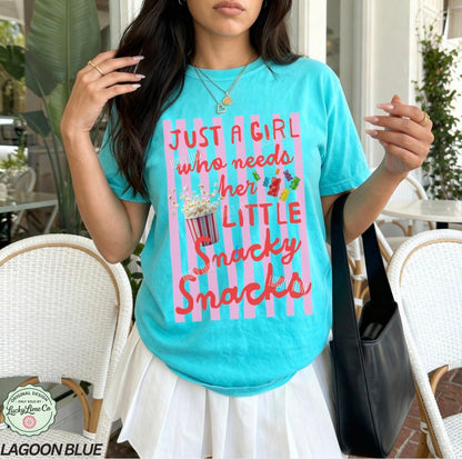 Woman wearing a turquoise t-shirt with a colorful graphic and text, standing outdoors.