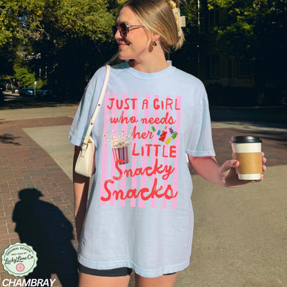 Woman wearing a light blue t-shirt with pink text and graphics, holding a coffee cup on a sidewalk.