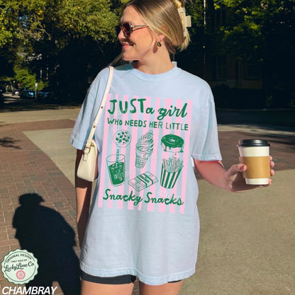 Woman wearing a light blue t-shirt with snack-themed design, holding a coffee cup outdoors.