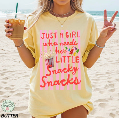 Woman on a beach wearing a yellow t-shirt with a snack-themed design, holding a drink.