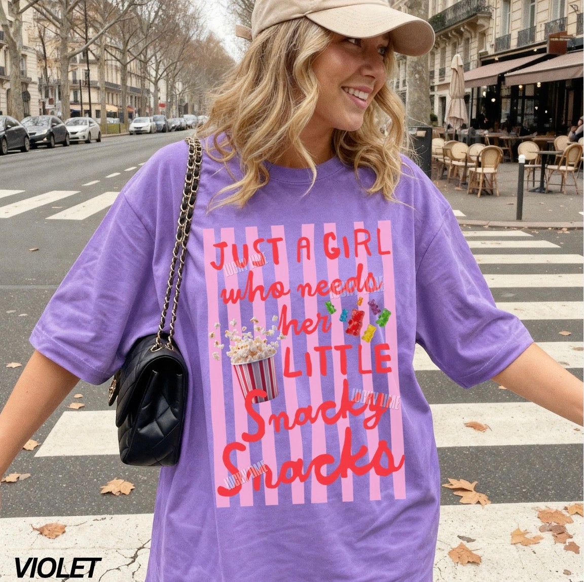 Woman wearing a purple t-shirt with text and a graphic, standing on a street.