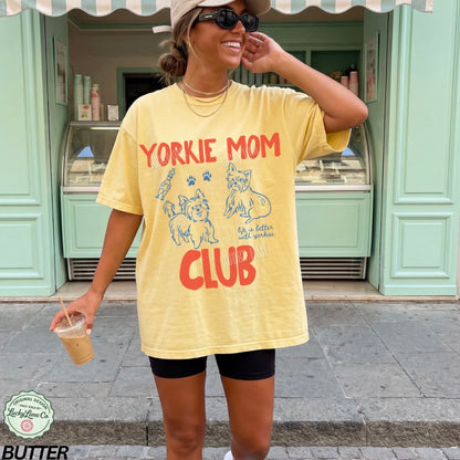 Woman wearing a yellow 'Yorkie Mom Club' t-shirt in front of a store.