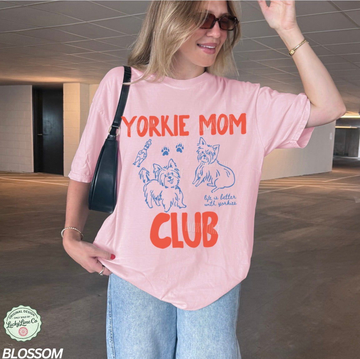 Person wearing a pink 'Yorkie Mom Club' t-shirt in an indoor setting
