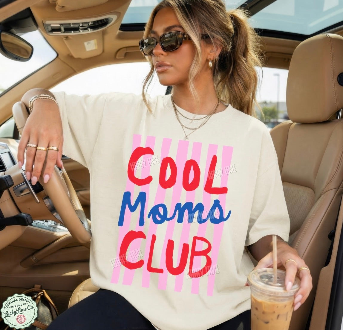 Woman sitting in a car wearing a 'Cool Moms Club' shirt and holding a drink.