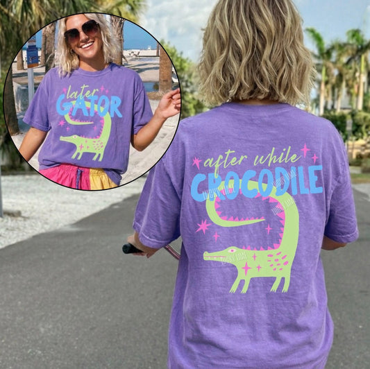 Person wearing a purple t-shirt with a crocodile graphic and text, standing outdoors.