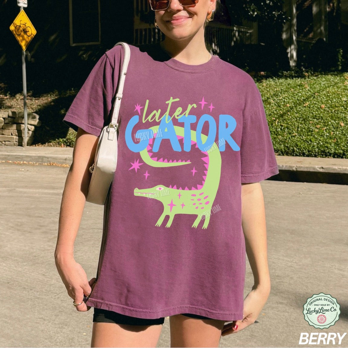 Person wearing a purple 'later GATOR' t-shirt with a green alligator graphic outdoors.