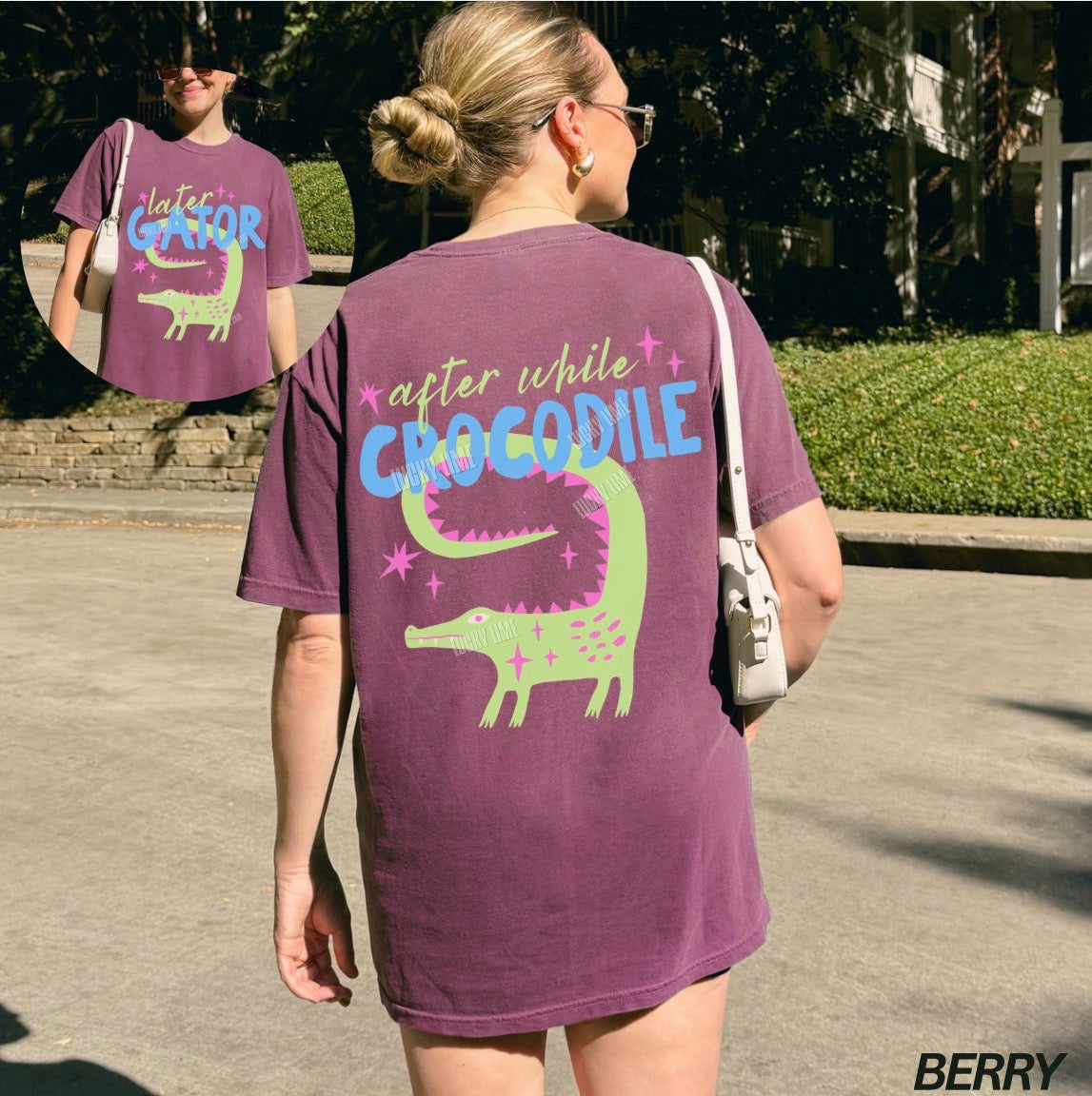 Person wearing a purple t-shirt with a green alligator graphic and text outdoors.
