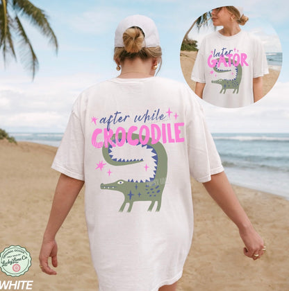 Person wearing a white t-shirt with a crocodile graphic and text on a beach.