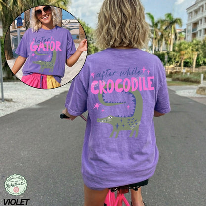 Woman wearing a purple t-shirt with a crocodile graphic and text, standing outdoors.