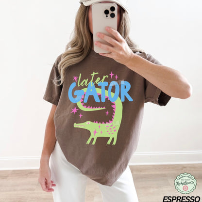 Person wearing a brown t-shirt with 'later GATOR' text and alligator graphic, taking a mirror selfie.