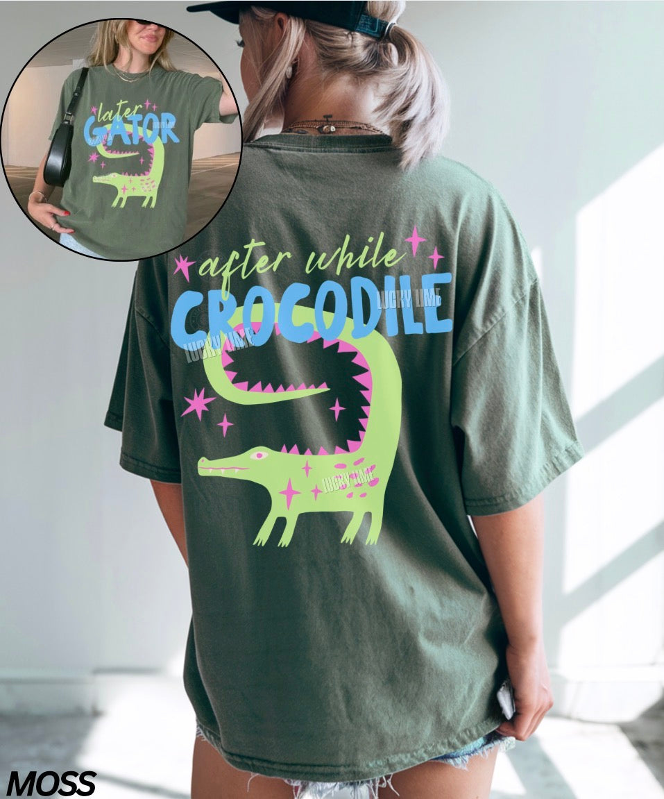 Person wearing a green t-shirt with a crocodile graphic and text, with a close-up inset of the shirt.