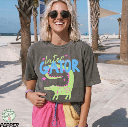 Person wearing a t-shirt with 'later gator' design on a beach