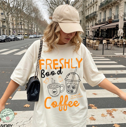 Person wearing a white t-shirt with 'Freshly Bood Coffee' text and graphics on a city street.