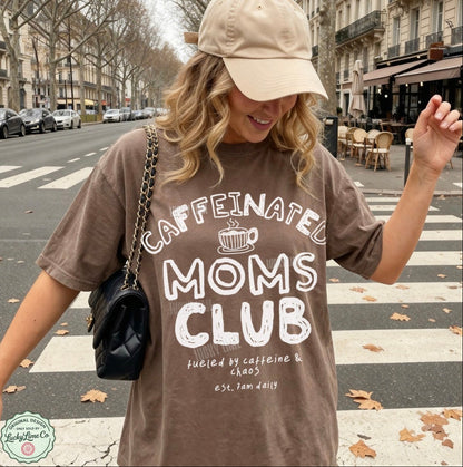 Woman wearing a 'Caffeinated Moms Club' t-shirt on a city street.