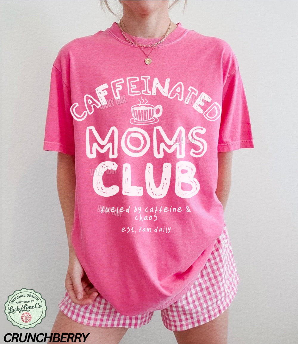 Person wearing a pink 'Caffeinated Moms Club' t-shirt and checkered shorts on a plain background