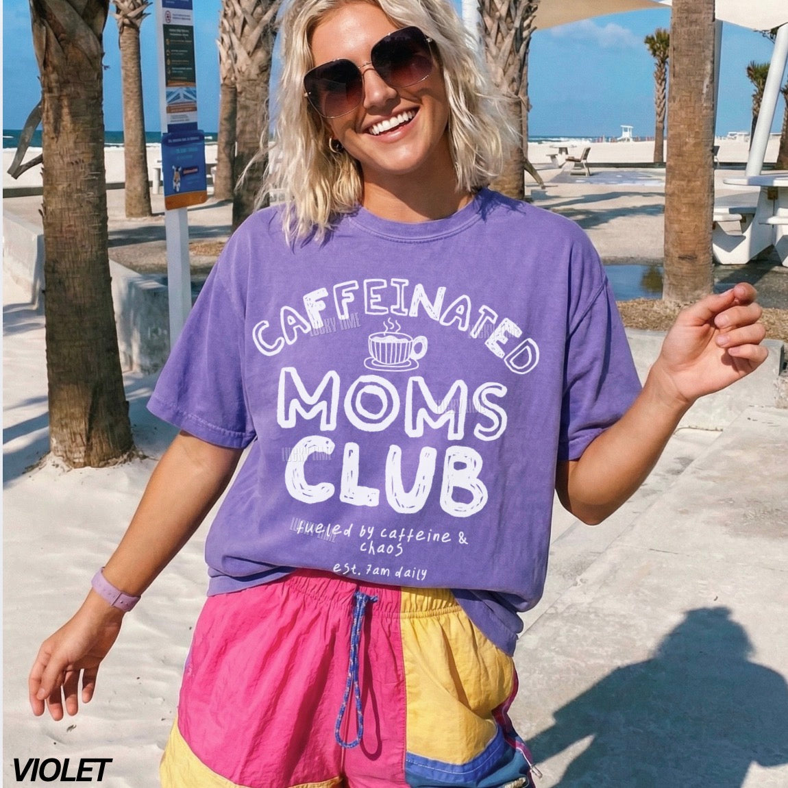 Woman wearing a purple 'Caffeinated Moms Club' t-shirt at a beach.