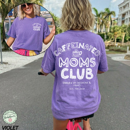 Person wearing a purple 'Caffeinated Moms Club' t-shirt with a scenic background.