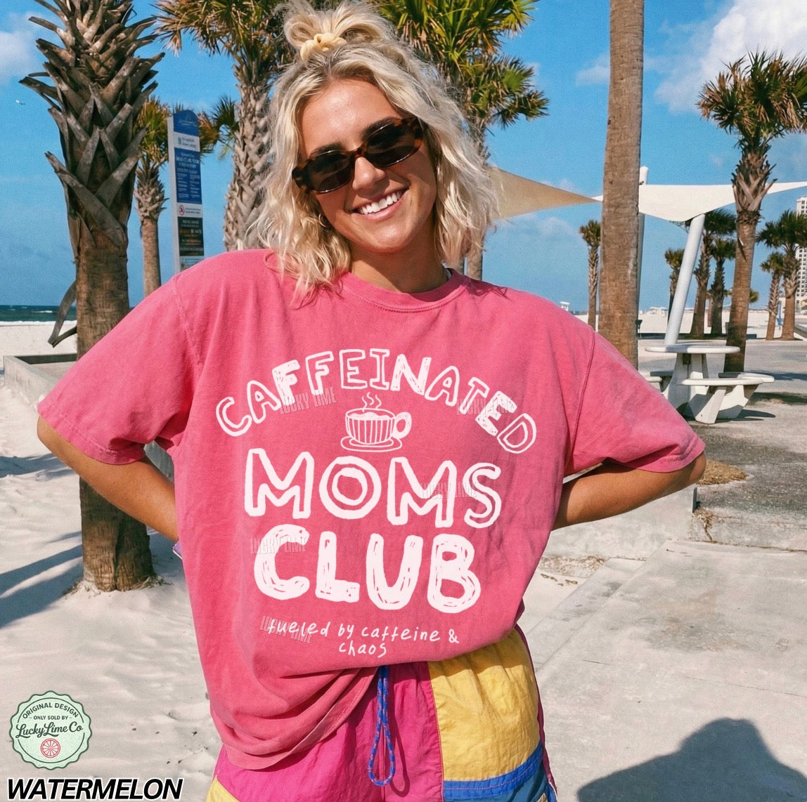 Woman wearing a pink 'Caffeinated Moms Club' t-shirt at a beach.