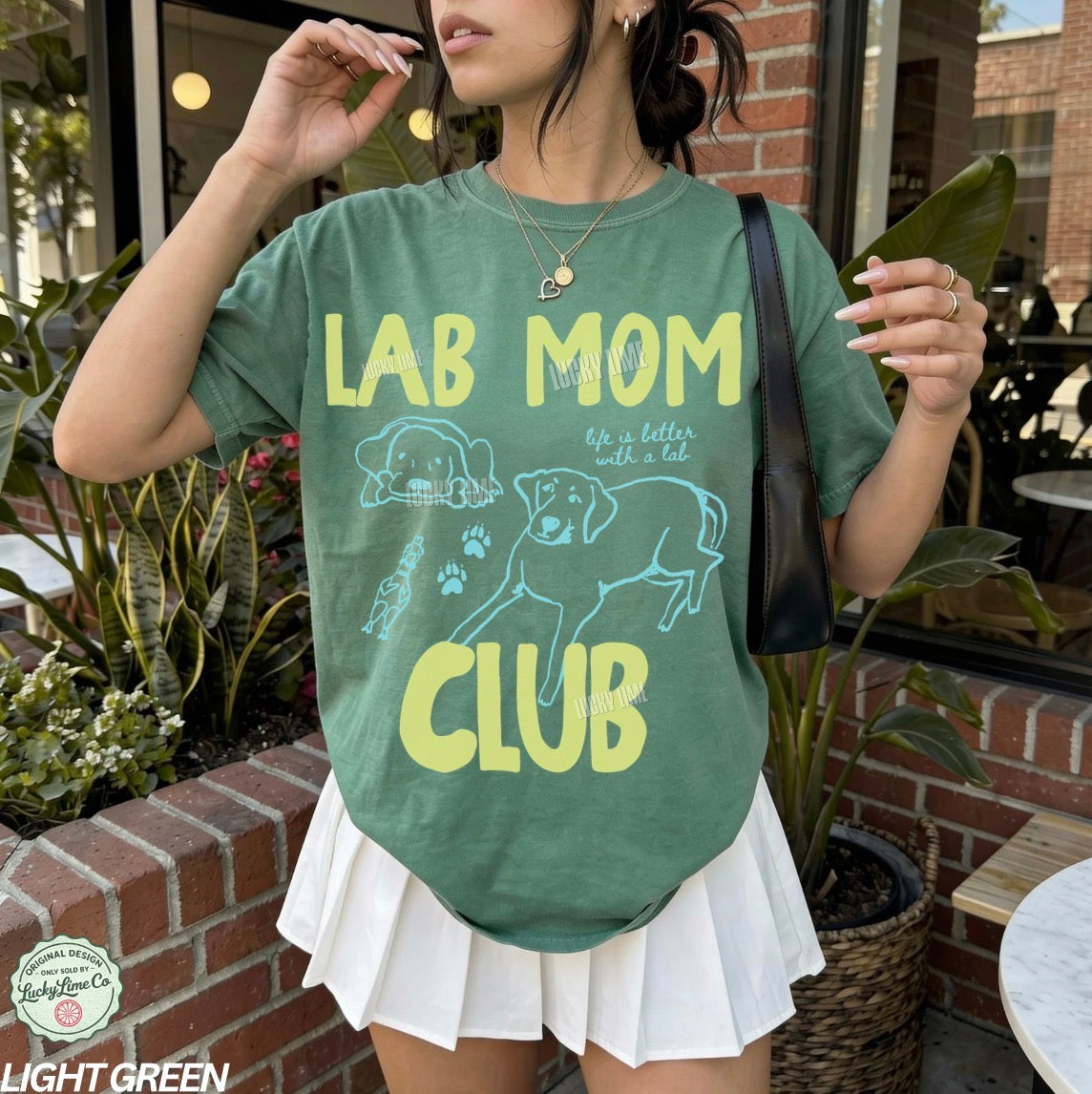 Person wearing a green t-shirt with 'Lab Mom Club' text and dog graphics outdoors.