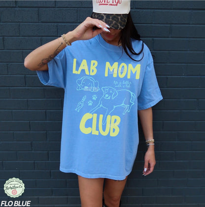 Person wearing a blue t-shirt with 'Lab Mom Club' text and graphics against a dark brick wall.