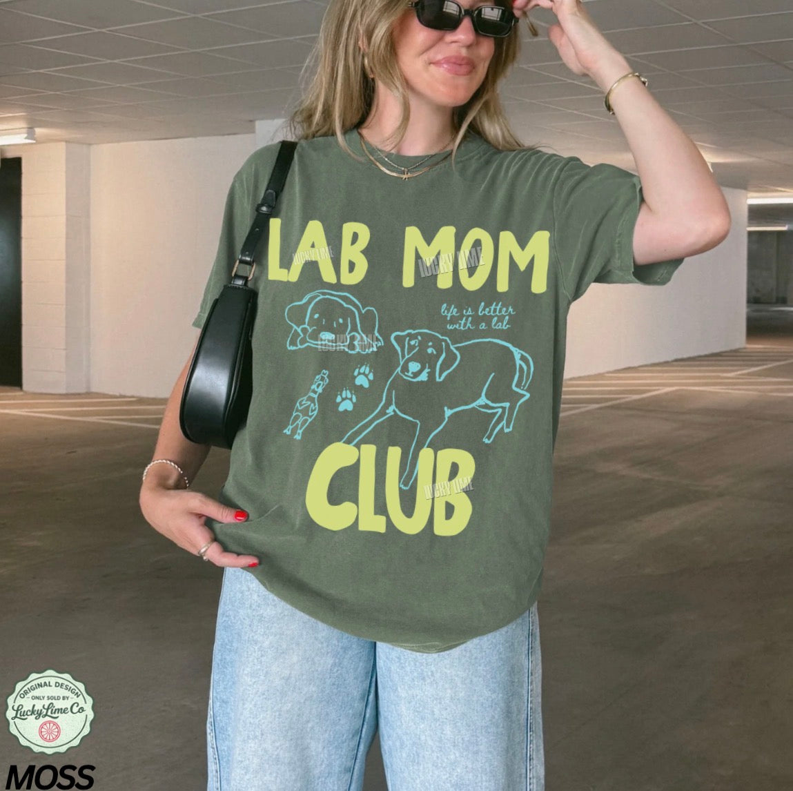 Woman wearing a green t-shirt with 'Lab Mom Club' text and graphics in an indoor setting.
