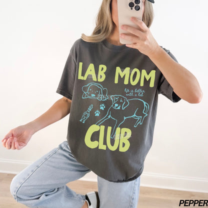 Person wearing a t-shirt with 'Lab Mom Club' text and graphics, taking a mirror selfie.