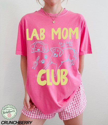 Person wearing a pink 'Lab Mom Club' t-shirt with checkered shorts on a plain background