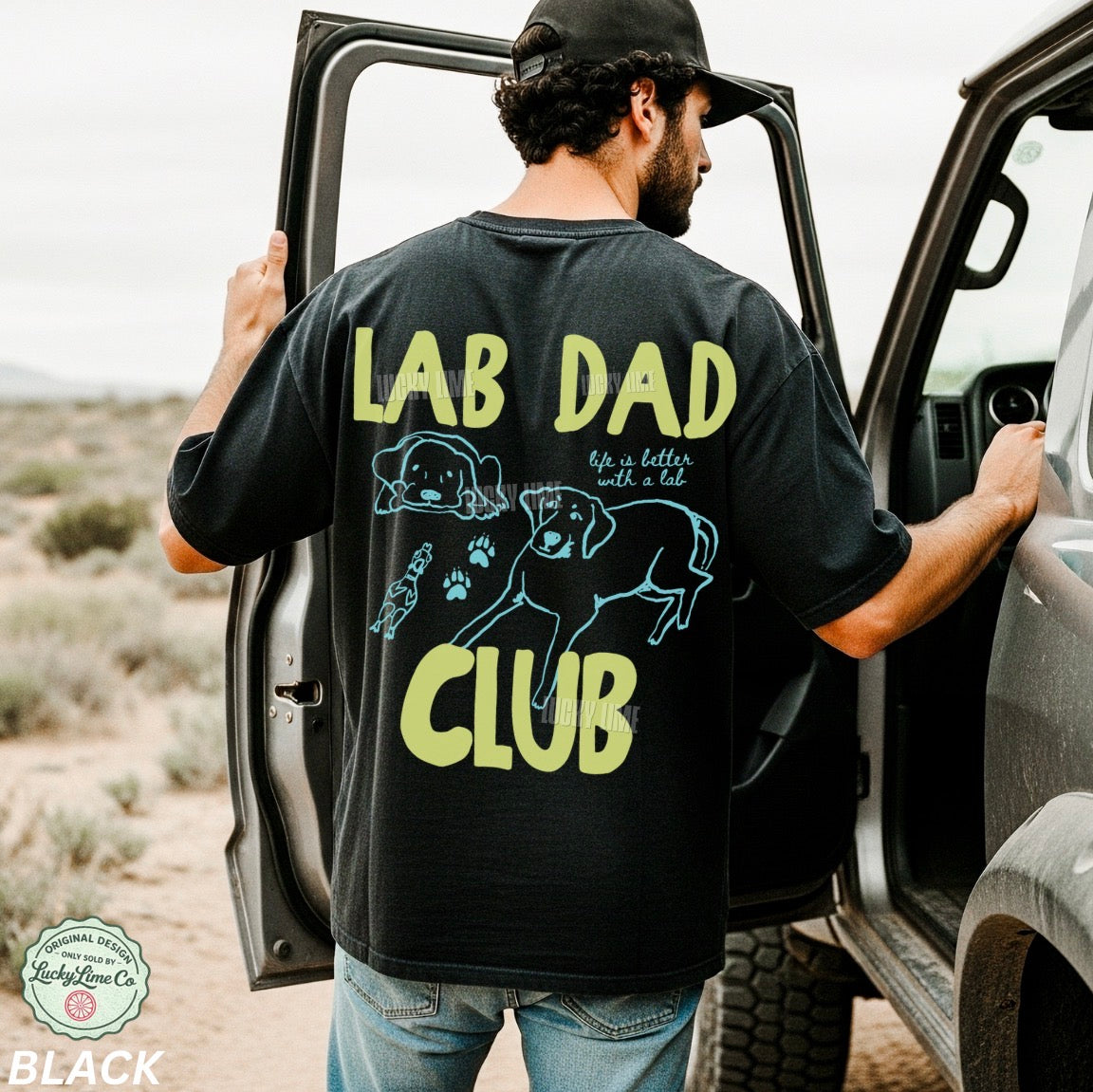 Man wearing a black t-shirt with 'LAB DAD CLUB' text and graphics, standing next to an open car door in a desert setting.