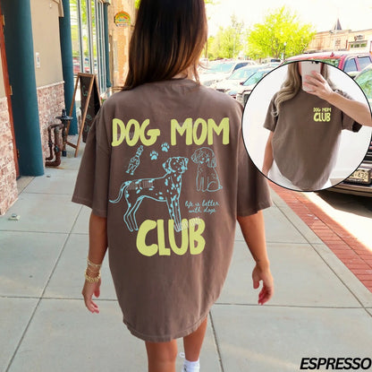 Person wearing a brown 'Dog Mom Club' t-shirt with graphic designs outdoors.