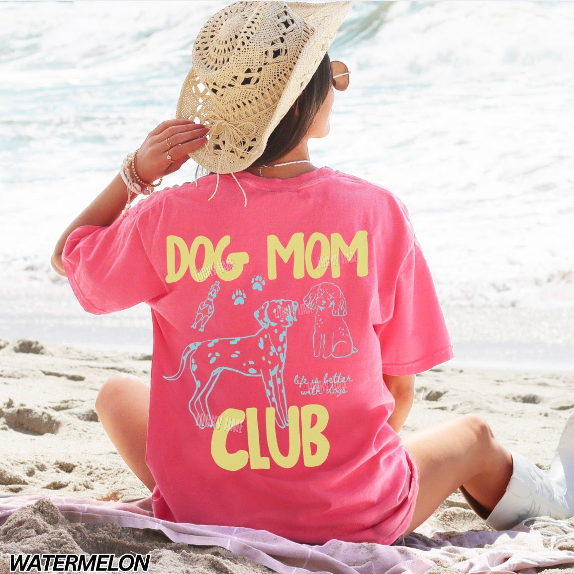 Person wearing a pink 'Dog Mom Club' t-shirt on a beach.