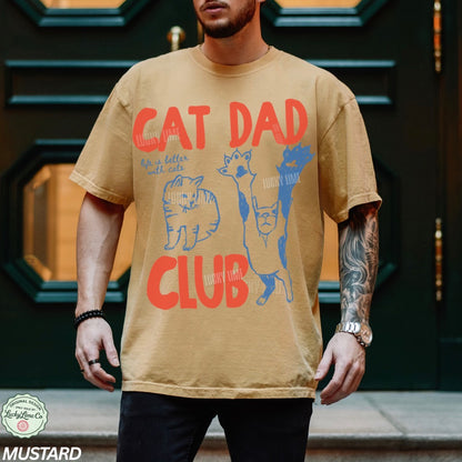Man wearing a beige t-shirt with 'Cat Dad Club' design in front of a dark door.