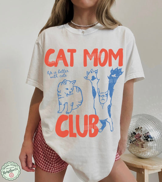 Person wearing a white t-shirt with 'Cat Mom Club' text and graphics, standing against a neutral background.