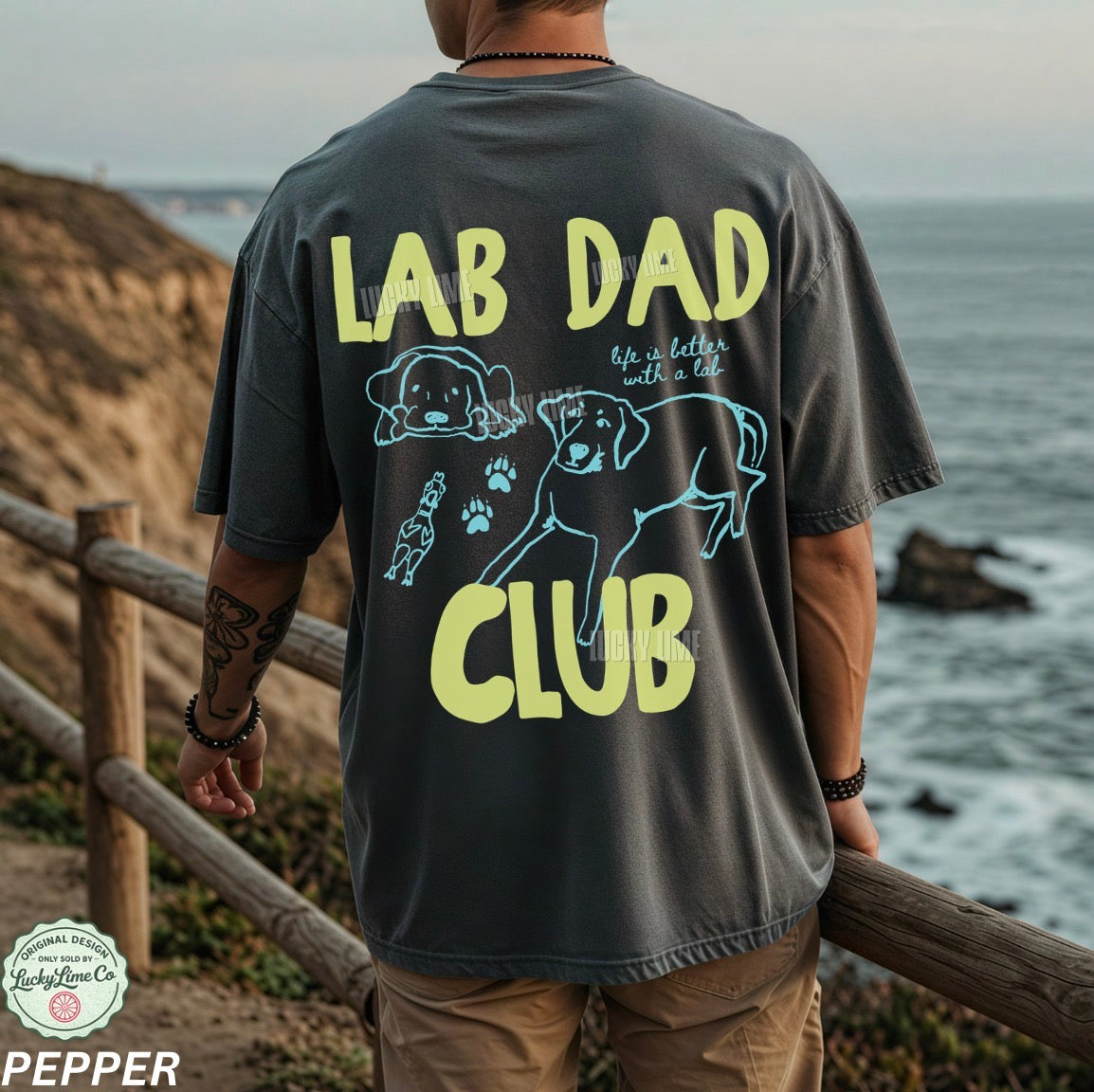 Person wearing a 'Lab Dad Club' t-shirt by the ocean