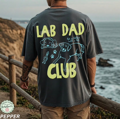 Person wearing a 'Lab Dad Club' t-shirt by the ocean