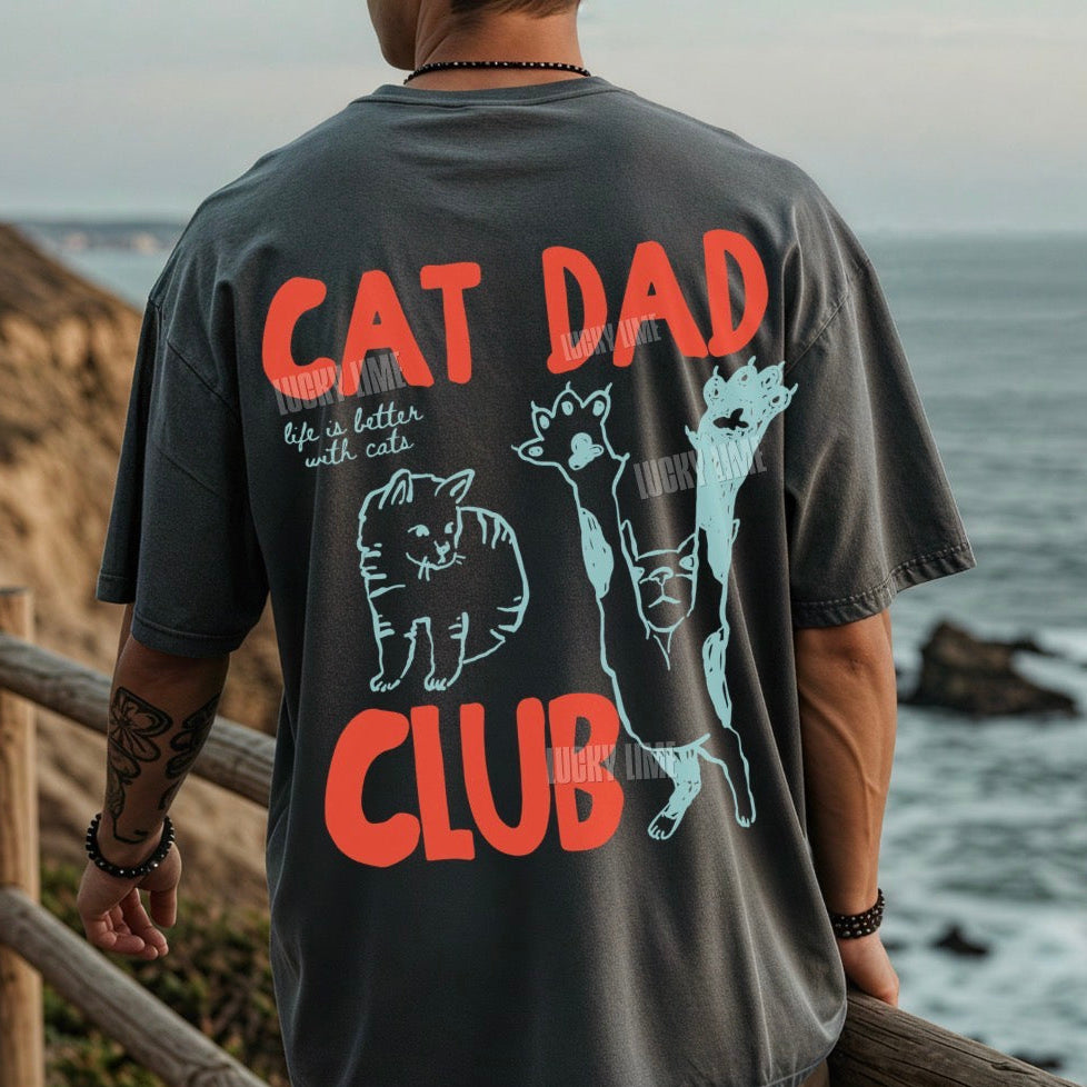 Person wearing a t-shirt with 'Cat Dad Club' design by the ocean.