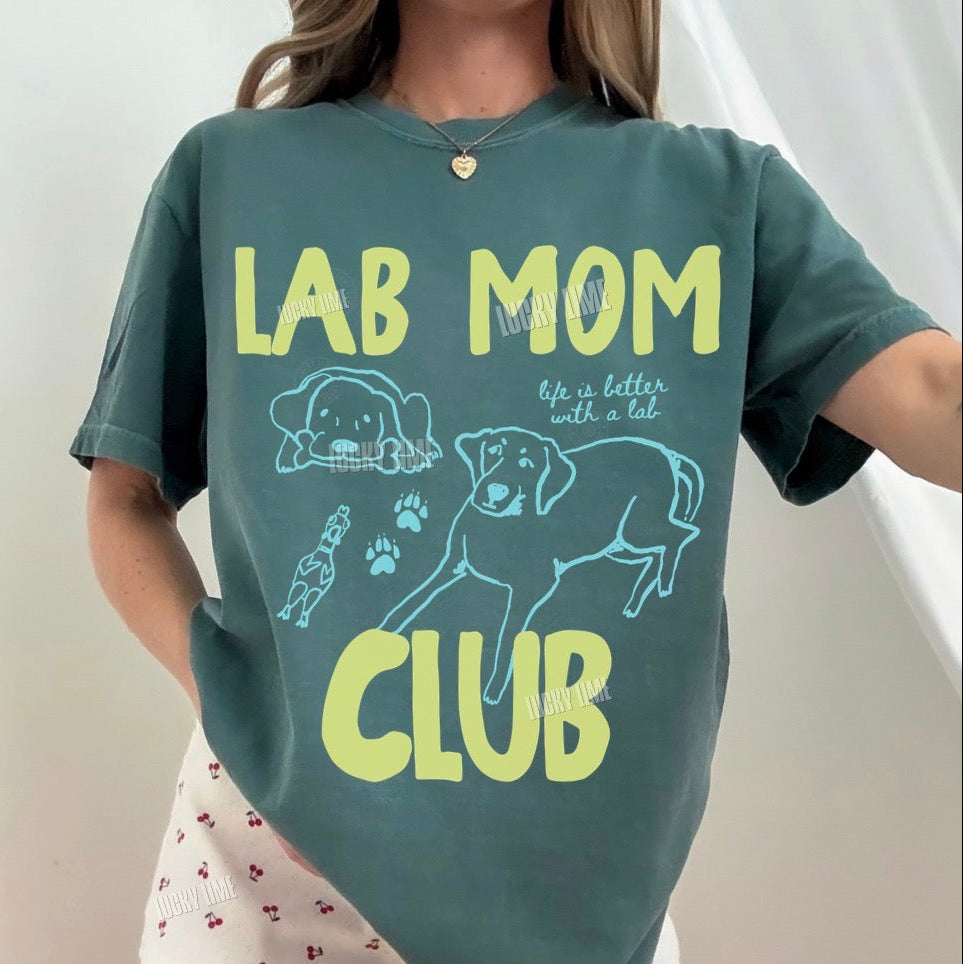 Person wearing a green t-shirt with 'Lab Mom Club' text and dog graphics on a plain background.