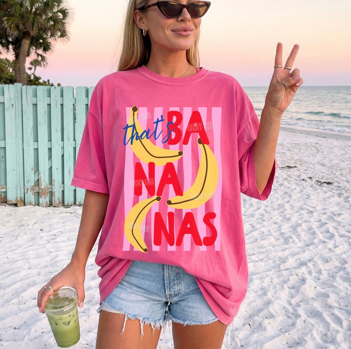 Woman on a beach wearing a pink t-shirt with banana graphics and text.