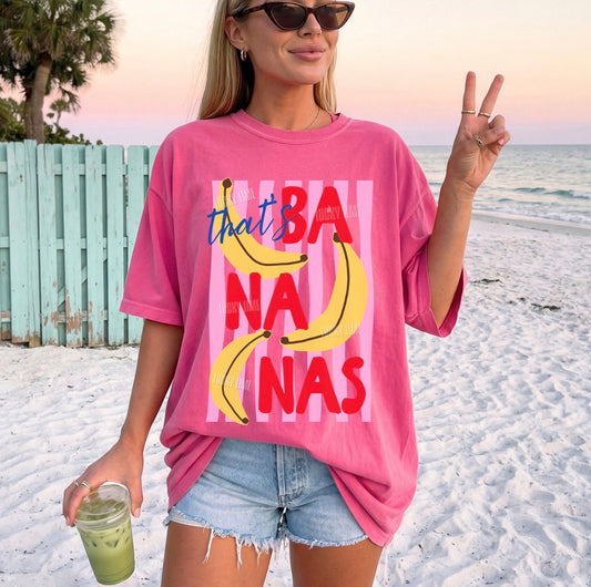 Woman on a beach wearing a pink t-shirt with banana graphics and text.