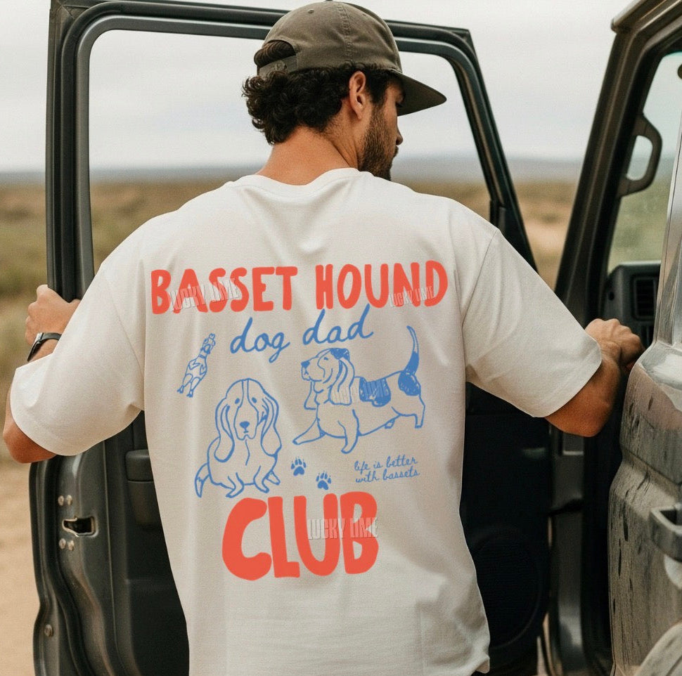 Man wearing a 'Basset Hound Dog Dad Club' shirt standing next to an open car door in a desert setting.