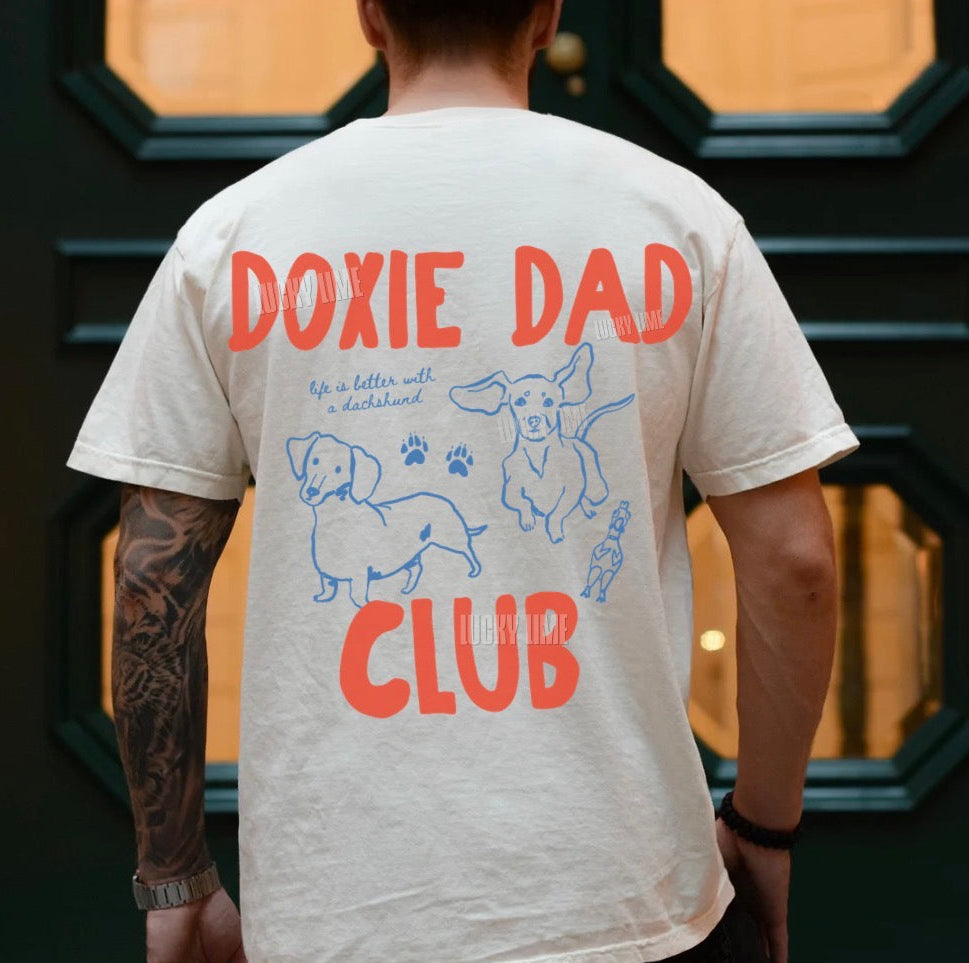 Person wearing a t-shirt with 'Doxie Dad Club' design in front of a decorative door.
