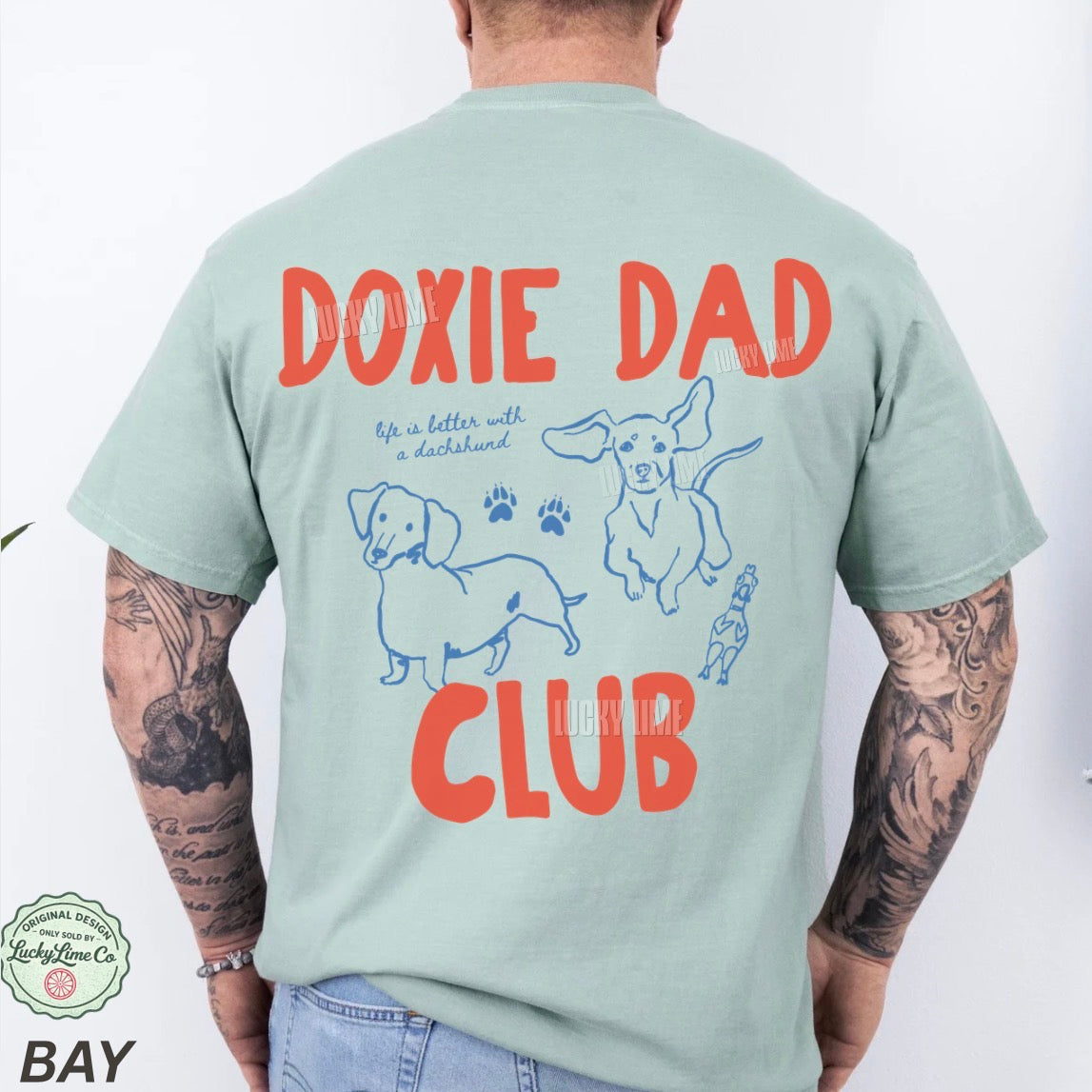 Person wearing a light green t-shirt with 'Doxie Dad Club' text and dog illustrations on the back.