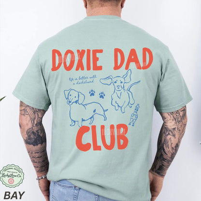 Person wearing a light green t-shirt with 'Doxie Dad Club' text and dog illustrations on the back.