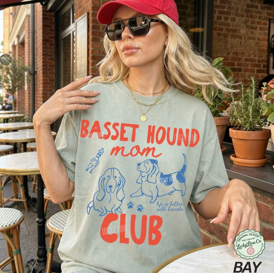 Woman wearing a t-shirt with 'Basset Hound Mom Club' design outdoors.
