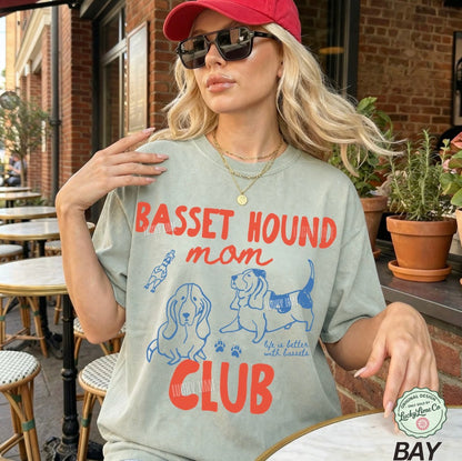Woman wearing a t-shirt with 'Basset Hound Mom Club' design outdoors.