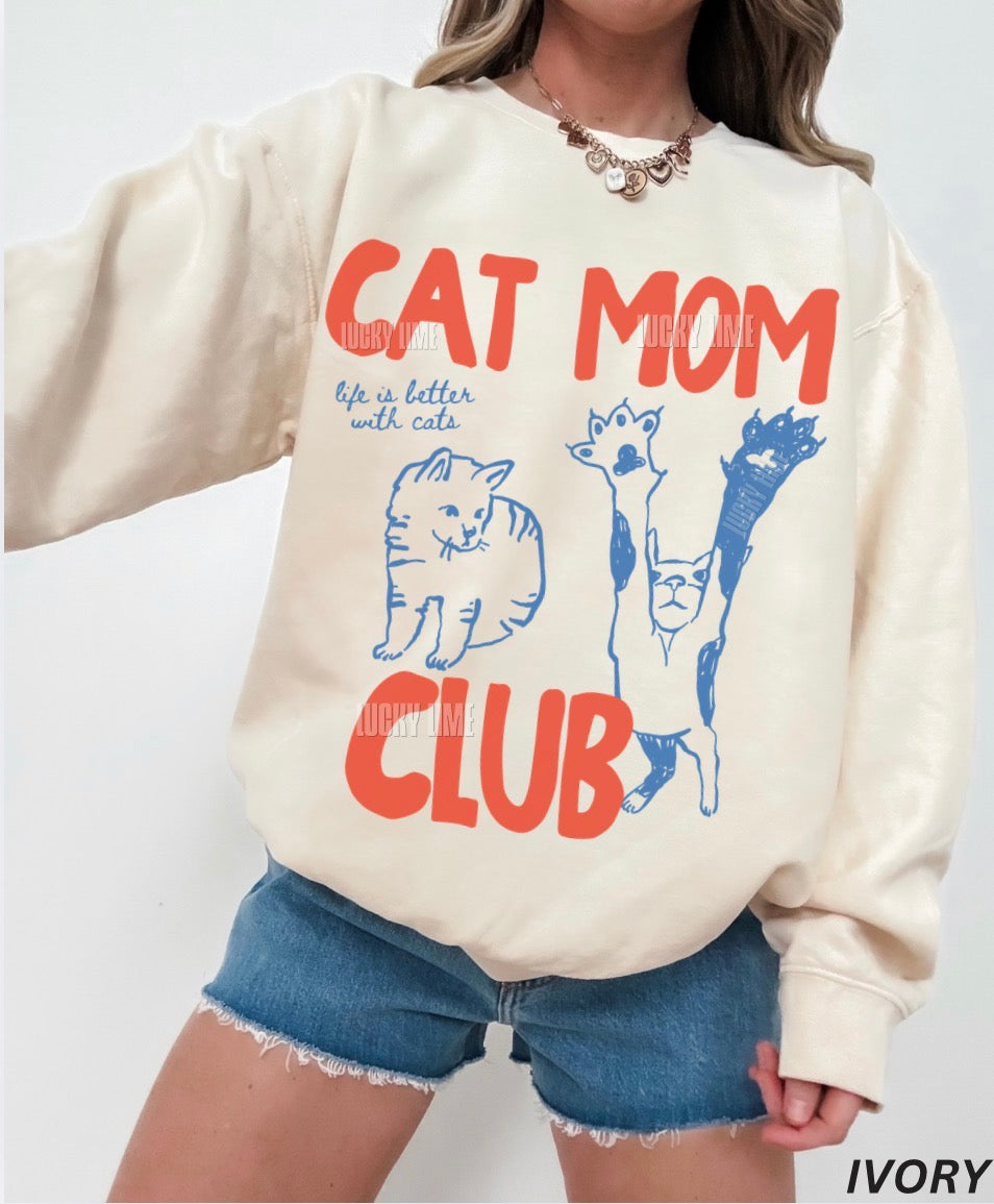 Person wearing a cream sweatshirt with 'Cat Mom Club' text and cat illustrations on a white background.