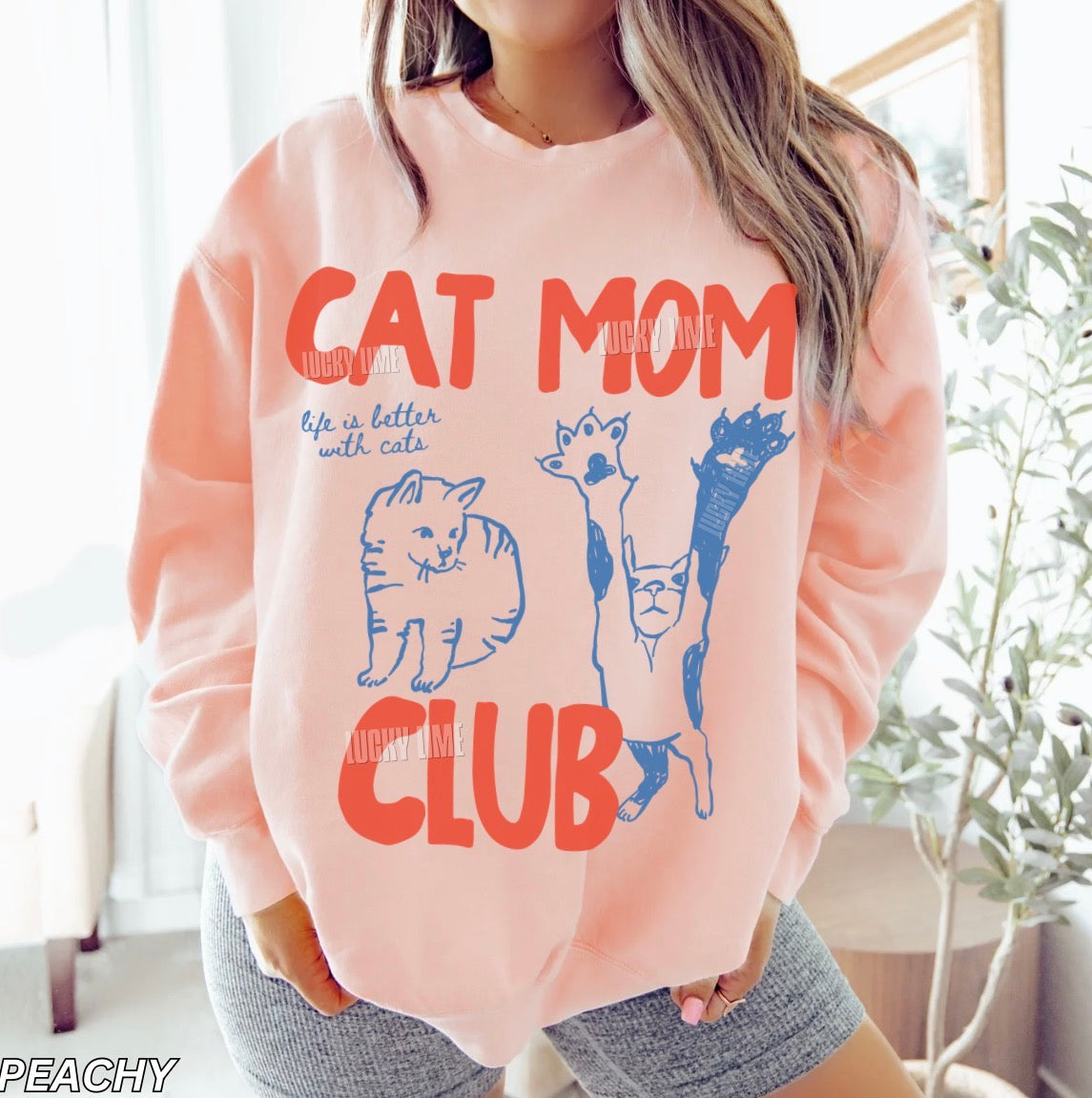 Person wearing a peach-colored sweatshirt with 'Cat Mom Club' text and cat illustrations.