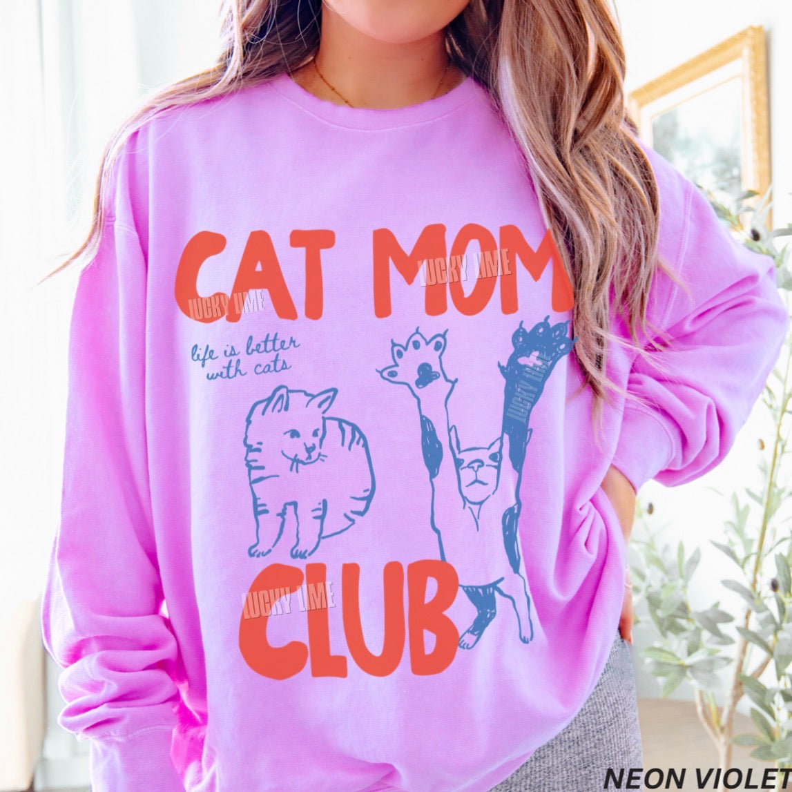 Person wearing a pink sweatshirt with 'Cat Mom Club' text and cat illustrations.