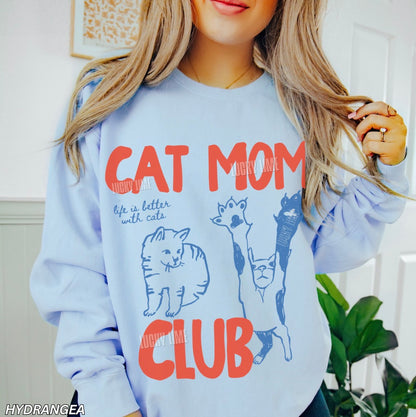 Light blue sweatshirt with 'Cat Mom Club' text and cat illustrations worn by a person.