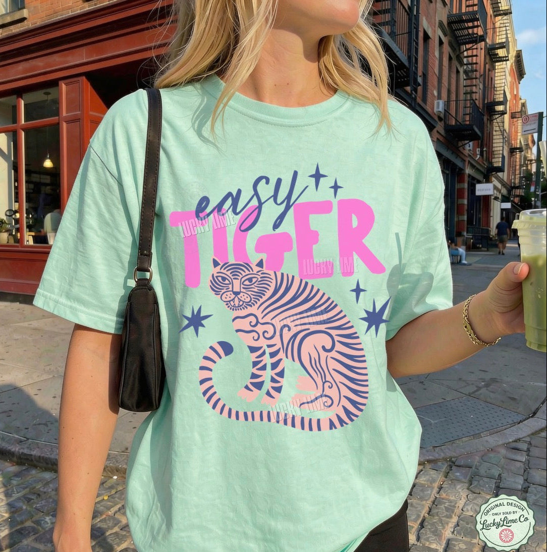 Woman wearing an island reef green shirt with “easy tiger” and a tiger graphic standing on a street outside