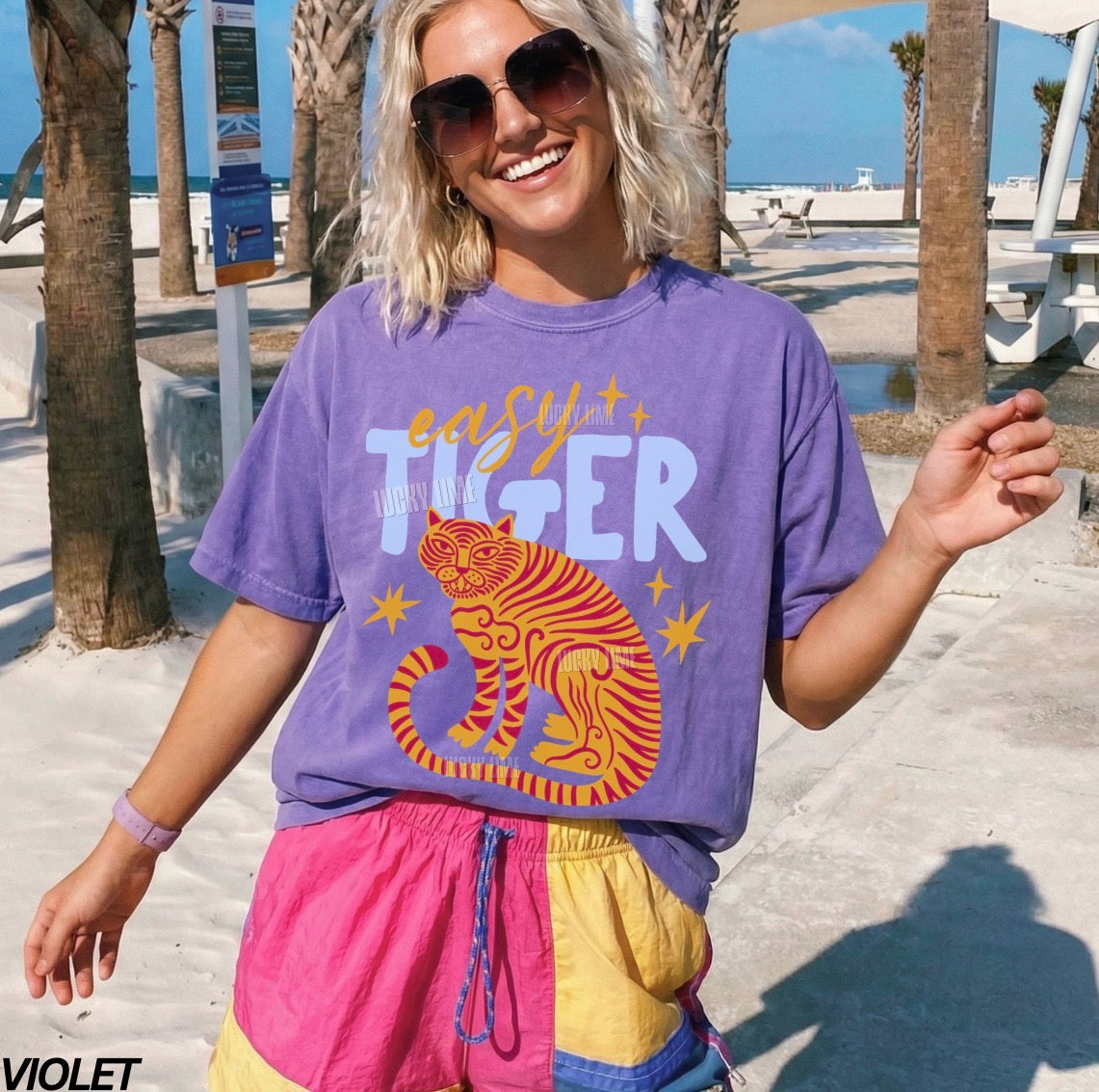 Person wearing a purple 'Easy Tiger' t-shirt at a beach.